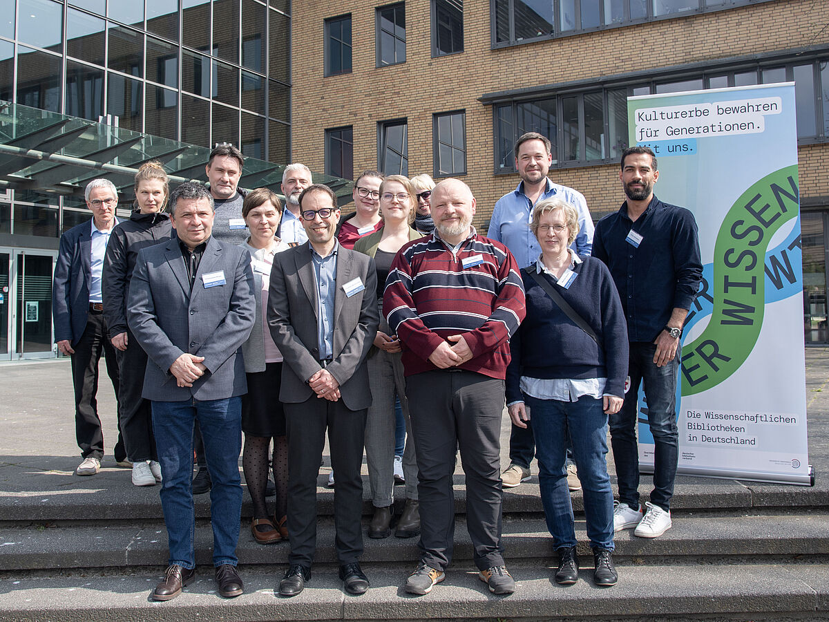 Group photo of the Team In terris Gryphi made up of 14 people. In the background you can see a modern building built of yellow brick and glass.